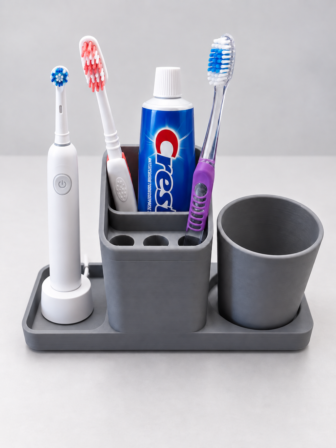 Gray bathroom sink organizer with toothpaste, two regular toothbrushes, an electric toothbrush and matching printed cup