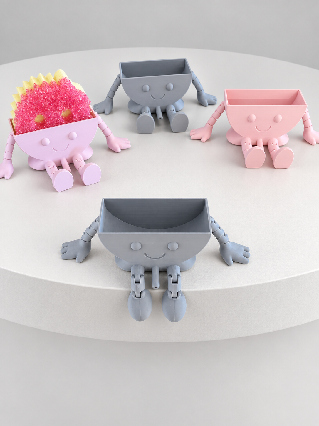 Four smiling Scrub Mommy/Daddy holders in gray and pink, with a sponge in one holder